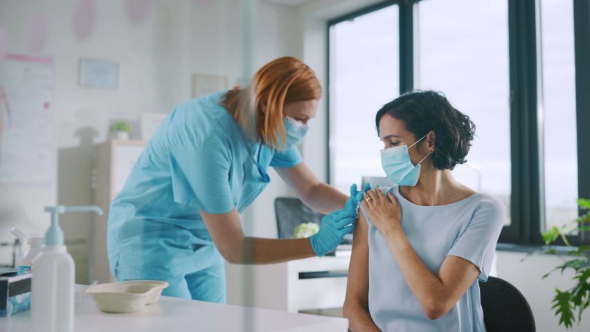 Medical Nurse in Safety Gloves and Protective Mask is Making a Vaccine Injection to a Female Patient in a Health Clinic. Doctor Uses Hypodermic Needle and a Syringe to Put a Shot of Drug as Treatment. Royalty-Free Stock Footage #1059073847