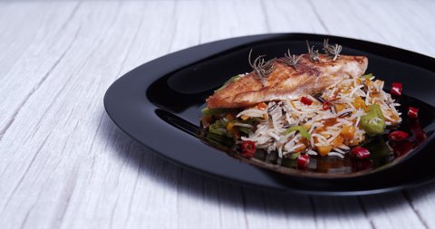 Grilled salmon with a rice and vegetable base accompanied by spicy chillies served on a black plate.