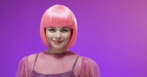 Portrait of Caucasian joyful stylish woman in pink wig smiling to camera on velvet background and blowing kisses. Close up of happy girl dancing. Extraordinary female charm. Barbie doll look concept.