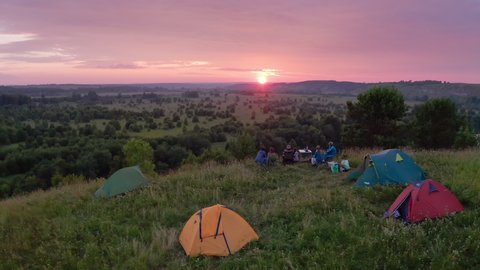 Camping family aerial. Extended family sit on the coast of the river with hiking camps set around and enjoy gentle sunset.