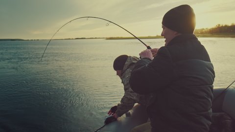 Friends fishing. Two amateur anglers fishing from the boat and fighting with trophy fish. Fishing rod bends under the big fish