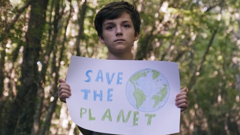 Save the planet poster protest boy holding in front of him in forest and looking at camera slow motion. Defender of nature. Children protect nature. Parenting. Childhood. Ecology. Green planet earth
