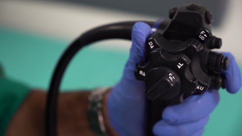 The doctor's hand in blue glove controls the endoscope. 