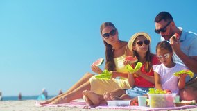 family, leisure and people concept - happy mother, father and two daughters having picnic on summer beach and eating watermelon - Powered by Shutterstock - Get 15% off with code: PIKWIZARD15