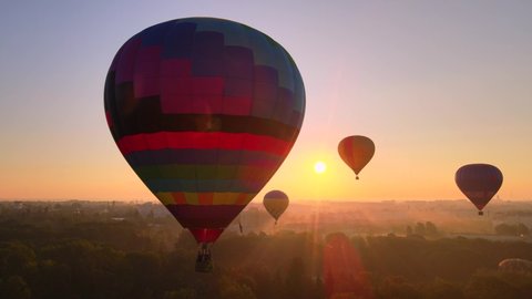 Aerial drone view of colorful hot air balloon flying over green park and river in small european city at summer sunrise, Kiev region, Ukraine