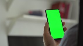 Handheld Camera: Point of View of Man at Modern Room Sitting on a Chair Using Phone With Green Mock-up Screen Chroma Key Surfing Internet Watching Content Videos Blogs