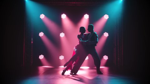 Silhouette of dancers in a smoky ballroom. Passionate couple dancing tango in a dark room with spotlights in slow motion.