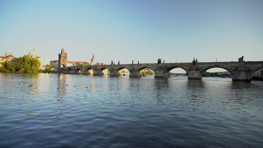 
stone Charles Bridge from the 14th century in the center of Prague and the flowing surface of the Vltava River in the center of Prague at sunset. blue sky and sun shining