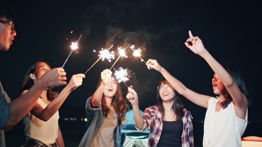 Group of young Asian college student friends lit light sparkler, sing and dance together at beach camping tent. Party people, love friendship relationship, or outdoor camping activity concept Royalty-Free Stock Footage #1059096788