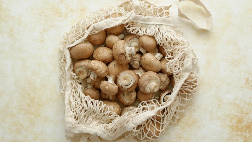 Young fresh Champignons in a ecological zero-waste net bag placed on beige background. Top view, flat lay.