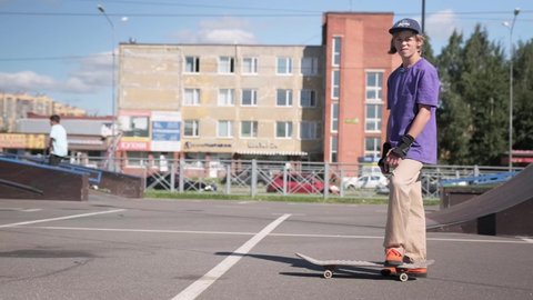 St.Petersburg, Russia, Aug, 2020; Young hipster teen in skate park rides his skateboard in Sunny weather. Person can perform various tricks on skateboard on sunny day against backdrop of skateboarders