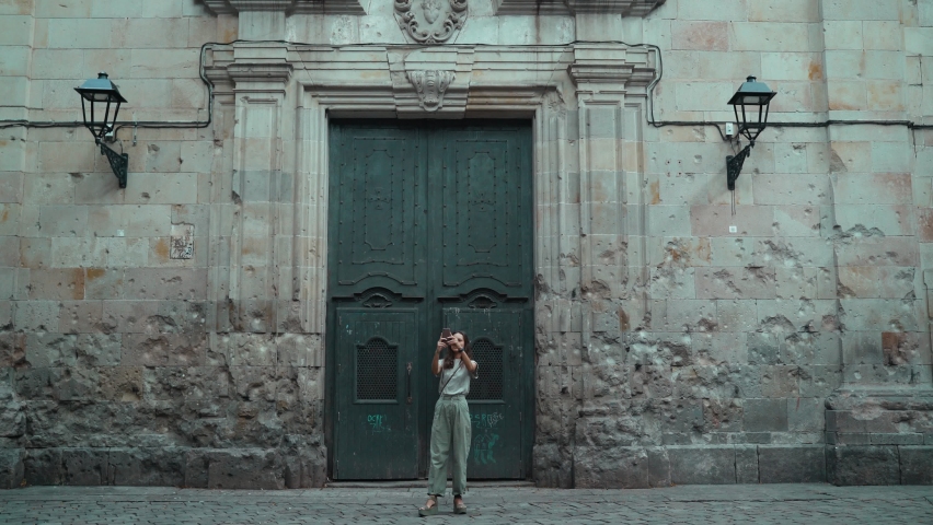 Beautiful long-haired brunette making photo in front of a large carved door. Young attractive woman taking pictures of stunning buildings. Pretty tourist makes selfie in a beautiful city.Mobile phone.