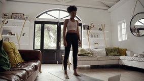 Sporty young African American woman with afro doing exercise on yoga mat while watching fitness video online on laptop at home