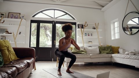 Sporty young African American woman with afro doing exercise on yoga mat while watching fitness video online on laptop at home