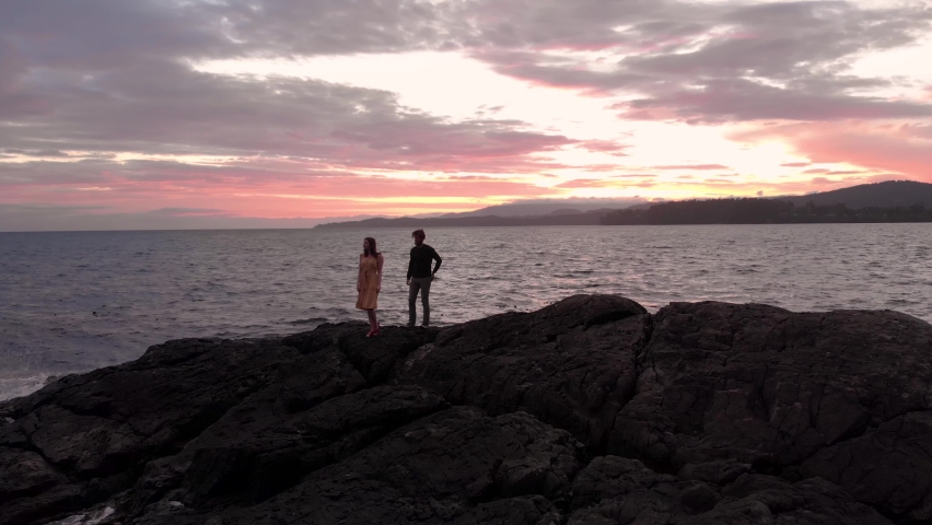 A attractive young man getting on his knee to propose to his girlfriend beside the ocean at sunset. 4k 24fps. Royalty-Free Stock Footage #1059106610