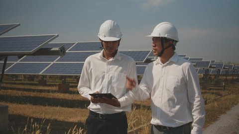 Technician and investor walking in Solar cell Farm through field of solar panels checking the panels at solar energy installation.Solar cells will be an important renewable energy of the future.