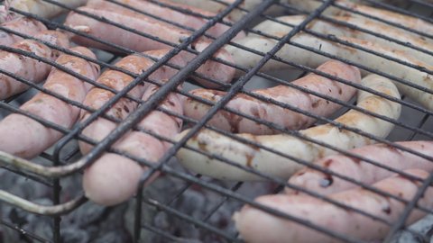 Cafes and restaurants, cooking, picnic, oriental kitchen concept - close-up cold cuts sausages on barbecue grill strung on skewer smoked and fried on roasted coals. Outdoor men's hand prepares to eat.