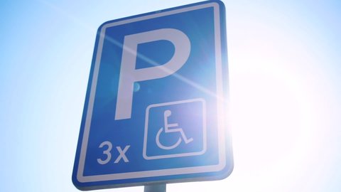 Disabled person parking sign on bright sun background. Special places for cars belonging disabled people. Wheelchair parking symbol.