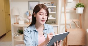 telework concept - Asian woman joins a video meeting by webcam and writes down information on digital tablet with ok gesture at home