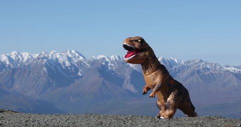 Beautiful installation outdoors on nature with prehistoric animal. Big dinosaur doll Tyrannosaurus Rex with person inside is dancing in mountains in amazing nature park. Inflatable doll.