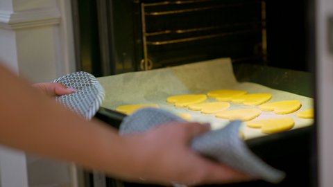 Woman puts baking sheet with cookies to the oven. Women's hands carry a baking tray with cookies to the oven. Housewife is baking sugar cookies. Cookies in the shape of hearts. Real time 4k footage