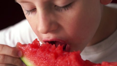 Close-up - a Caucasian boy greedily and hungry eats a ripe red juicy watermelon, watermelon juice flows down the child's face. selective focus, shallow depth of field