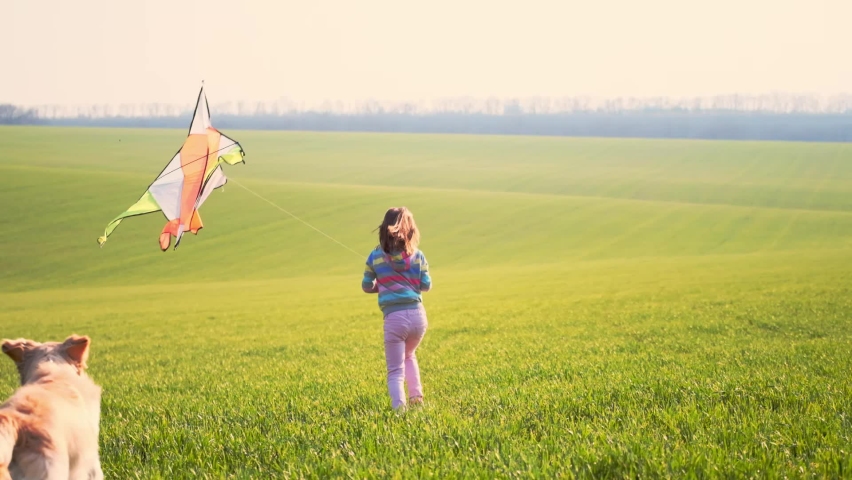 Beautiful little girl with cute dog flying kite on green spring field