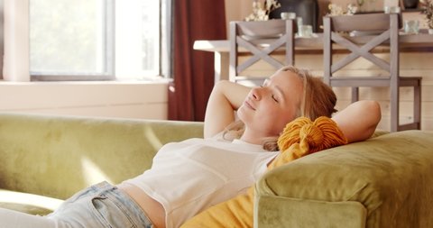 Young calm woman relaxing on comfortable sofa at home, resting on couch. Peaceful lady having daytime. Enjoy stress free at sweet home.