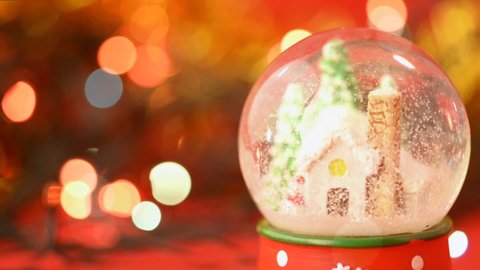 Beautiful Christmas glass  snow globe with a snowman a small house and Christmas trees on a blurry bokeh background of holiday garlands lights. Christmas and New Year  holiday celebrating concept