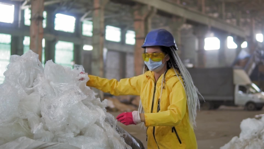 Waste processing plant. Technological process. Recycling and storage of waste for further disposal. Woman worker in hard hat gathering from the floor, pressing used plastic tape on recycle factory | Shutterstock HD Video #1059128174
