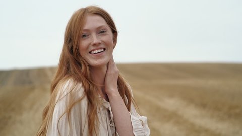 Natural Beauty Ginger Woman is running on golden Field happily, enjoying Nature. Amazing Woman touching her long Red Hair, smiling Charmingly. Looking Happy, feeling Liberty at Countryside. Emotions.