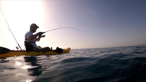 Mil Palmeras,Alicante Spain, September 14, 2020: Kayak fishing, trolling fishing. Underwater view of a oblade fish hooked to a lure being pulled out of water by a fisherman standing on a kayak 