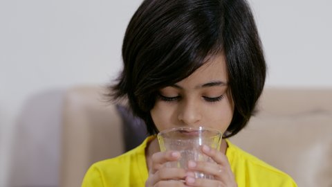 Closeup shot of an attractive little girl drinking a glassful of milk at home. Beautiful Indian child finishing a glass of milk and wiping her mouth with her hand - healthy food and drinks concept
