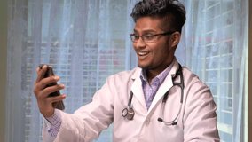 young asian doctor talking to smart shone camera in video chat.