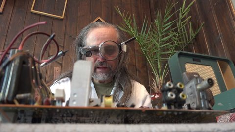 joke, humor, portrait of a mature mad man scientist in a white coat and funny glasses, toothless, repairs a computer board with a soldering iron and shows like