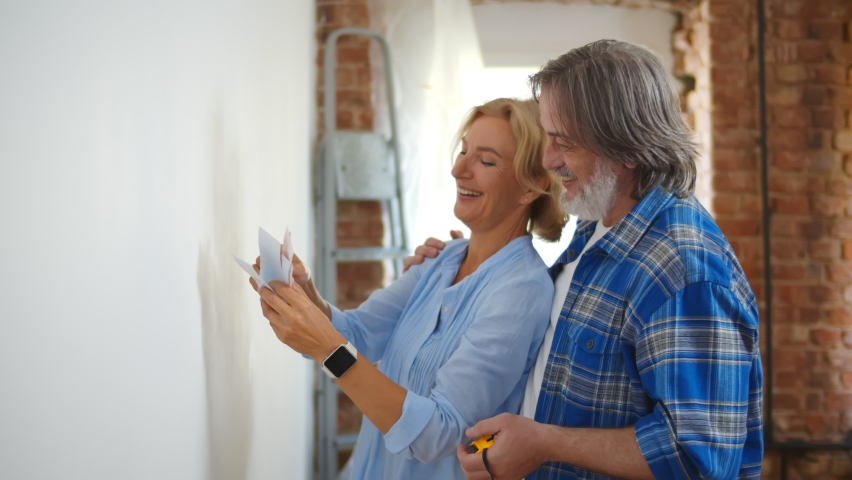 Senior couple with color swatch choosing painting for new home. Retired husband and wife selecting color for house redecoration. Elderly man and woman doing house improvement Royalty-Free Stock Footage #1059142754