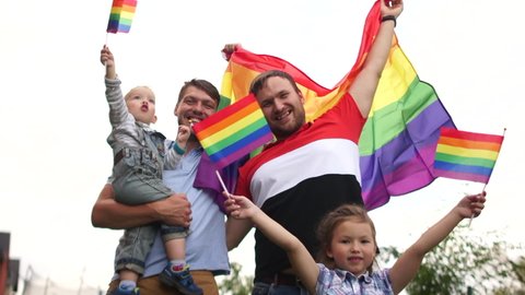 LGBT symbols. A happy homosexual family with two children is hugging each other near their house and waving rainbow flags