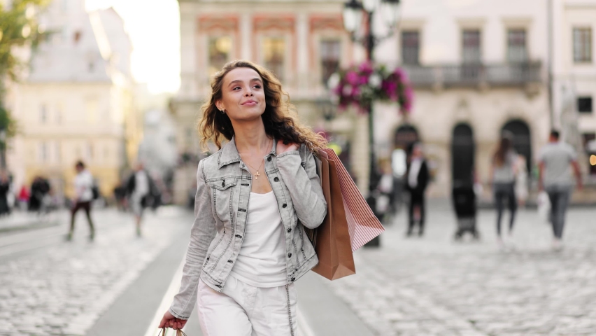 Gorgeous young woman in a denim jacket with different bags on her shoulder walking in a city at sunset. Slow motion. | Shutterstock HD Video #1059155507