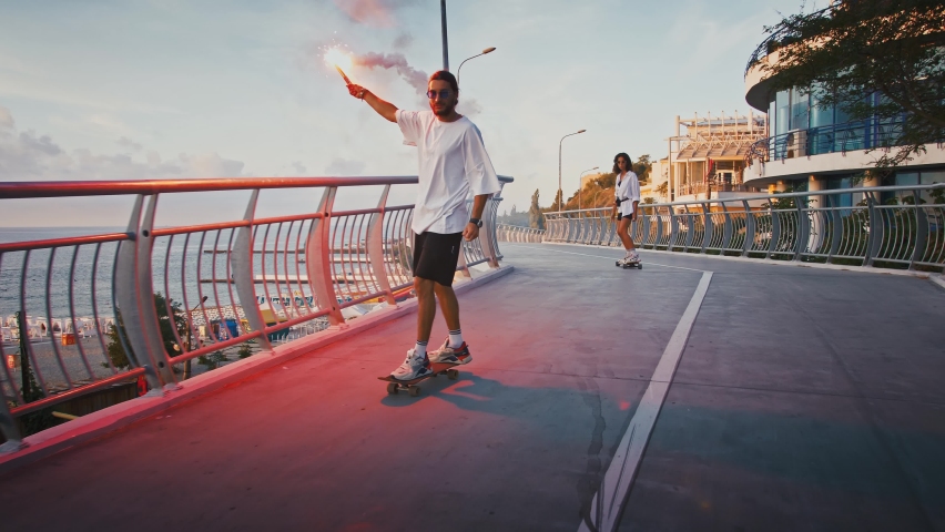 Millennial couple riding skateboard with red burning signal fire