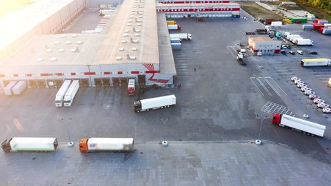 Logistics park with a warehouse - loading hub. Semi-trucks with freight trailers standing at the ramps for loading/unloading goods at sunset. Aerial hyper lapse (motion - time lapse)