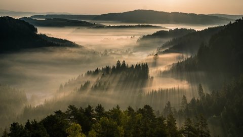 timelapse of morning sunrise in Adršpašsko teplické skály rocks natural reserve park protected area with sun rays shining trhought mist waves in the valley