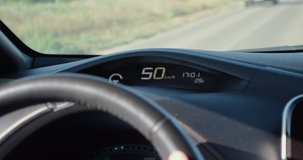 The speedometer of an electric car displays the speed of a car that is driving on a country road. The video was shot from behind the driver's shoulder.
