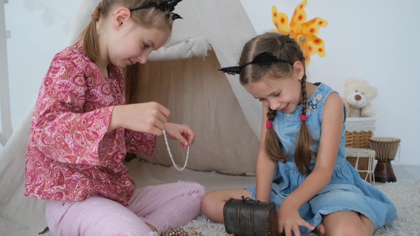 Girls kids exploring jewellery from treasure box sitting in front of wigwam in light room