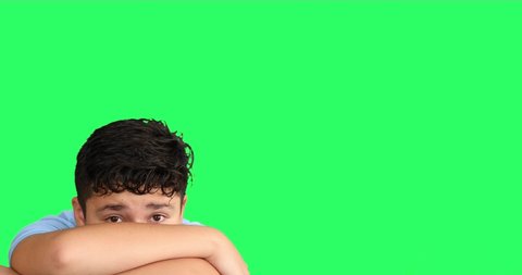 Scared young boy hiding his arms at green screen background