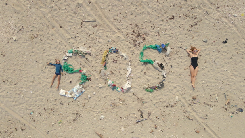 Aerial shot of the sign SOS made of trash on a beach. Woman lays by the sign simbolizing an exclamation mark. Ecologic disaster concept. Plastic pollution concept