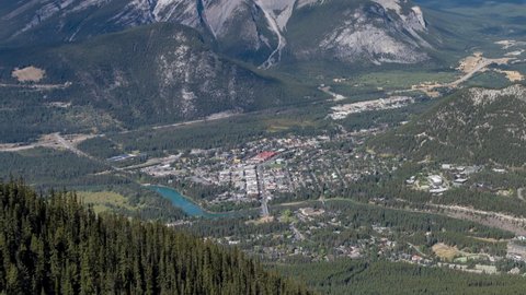 Town of Banff with surrounding mountains in summer time season sunny day. View from Sulphur Mountain summit observation deck. Alberta, Canada. Near to far zoom out Time-lapse 4K UHD.