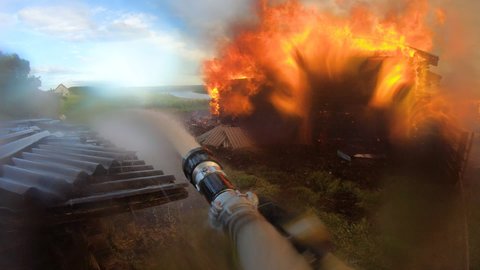 Big fire in the village.Burning of houses.Massive disaster. A firefighter bravely fights the fire. Extinguishing a fire with water.Fire element.Gopro.