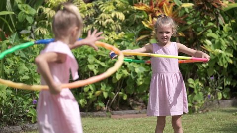 Young children sisters having fun with hula hoop outside in the park