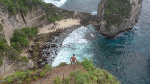 aerial view of a brave tourist standing on the edge of the cliff.Thousand islands viewpoint. Drone shot revealing Diamond beach Autah cliff and Batupabasan island, Nusa Penida