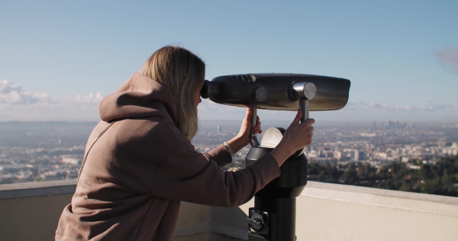 An attractive young woman looking through a telescope on a sunny day.